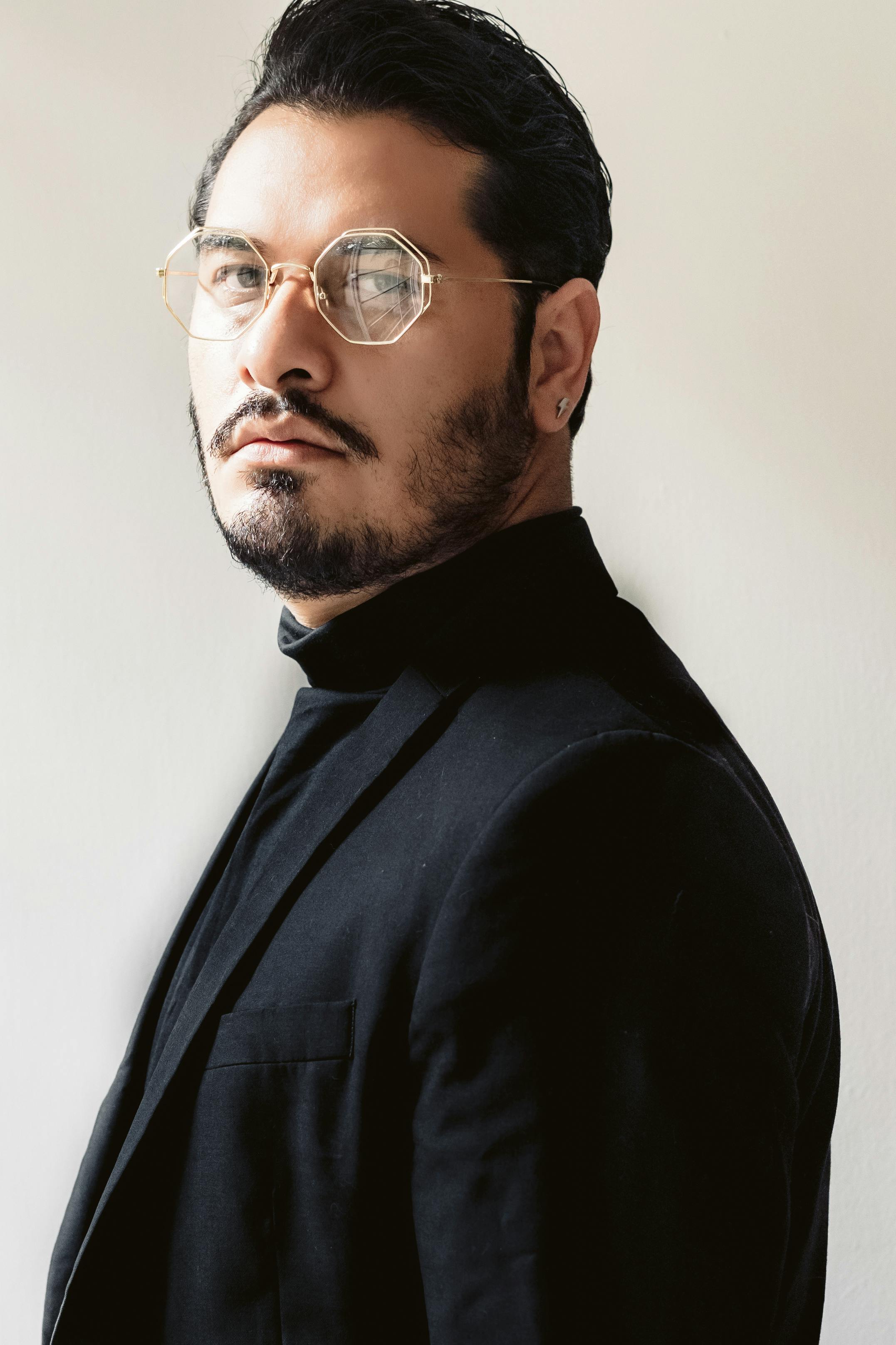Portrait of a stylish man in a black suit with eyeglasses, looking serious.
