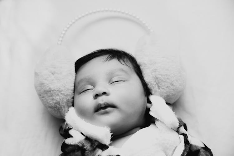 Grayscale Photo Of A Sleeping Baby Wearing Furry Earmuffs