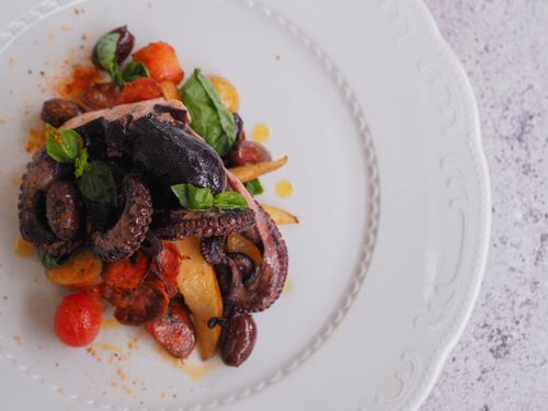 Free A delicious octopus dish served on a white plate with vegetables and herbs, captured from above. Stock Photo