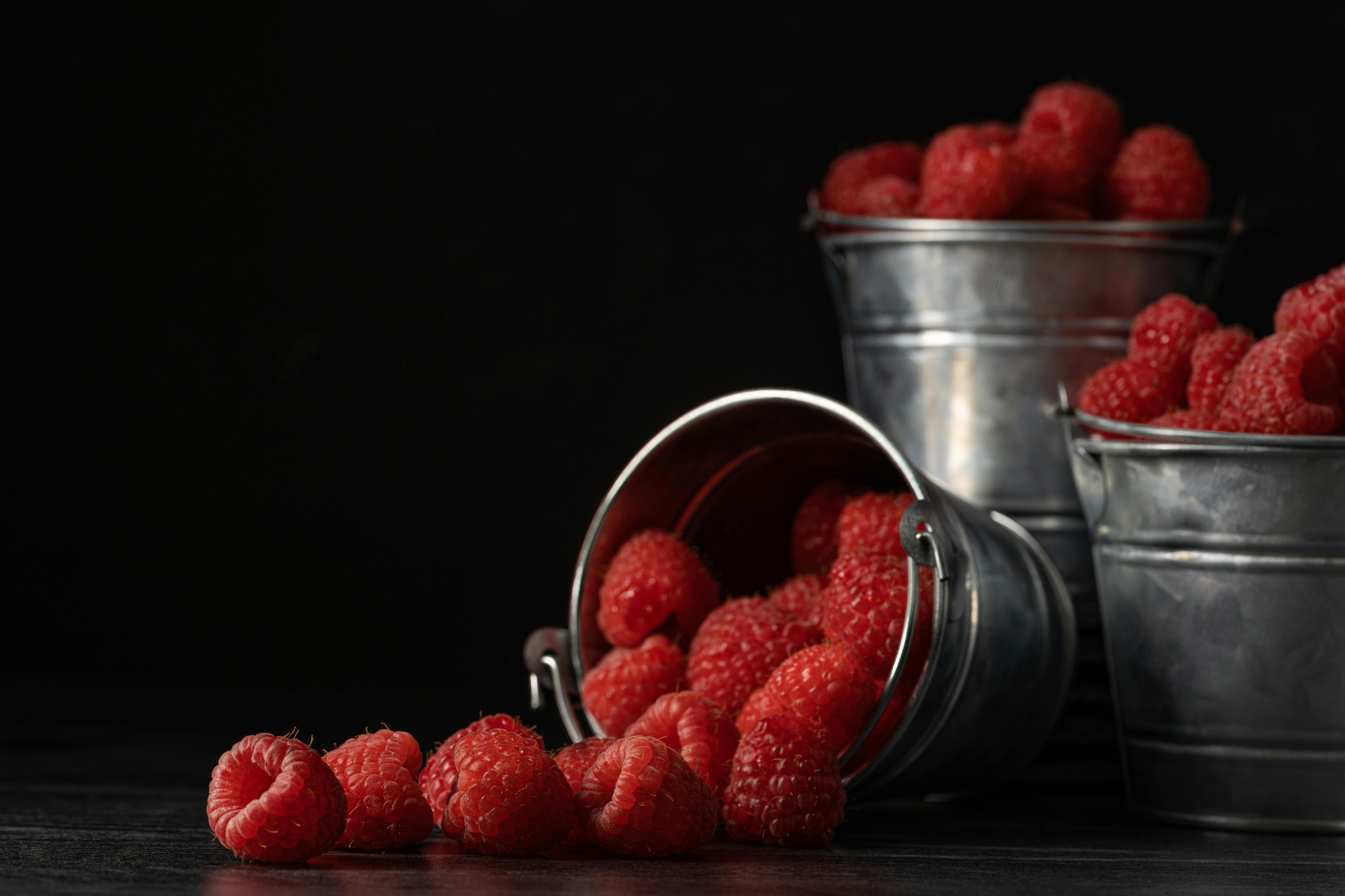 Close-up of fresh raspberries in metal buckets with a dark, dramatic background.