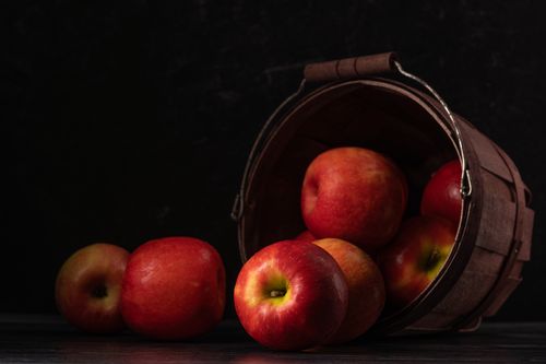 Free Red apples spill from a rustic wooden basket on a dark background, offering fresh and healthy fruit imagery. Stock Photo