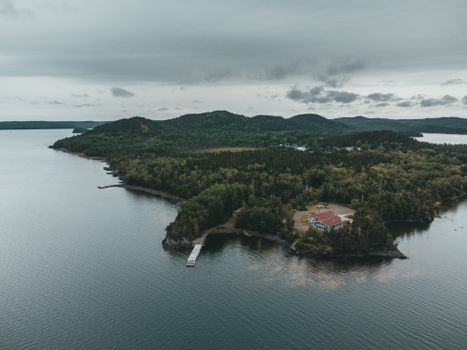 A serene aerial view of an island with a house, surrounded by a tranquil lake and lush forests.