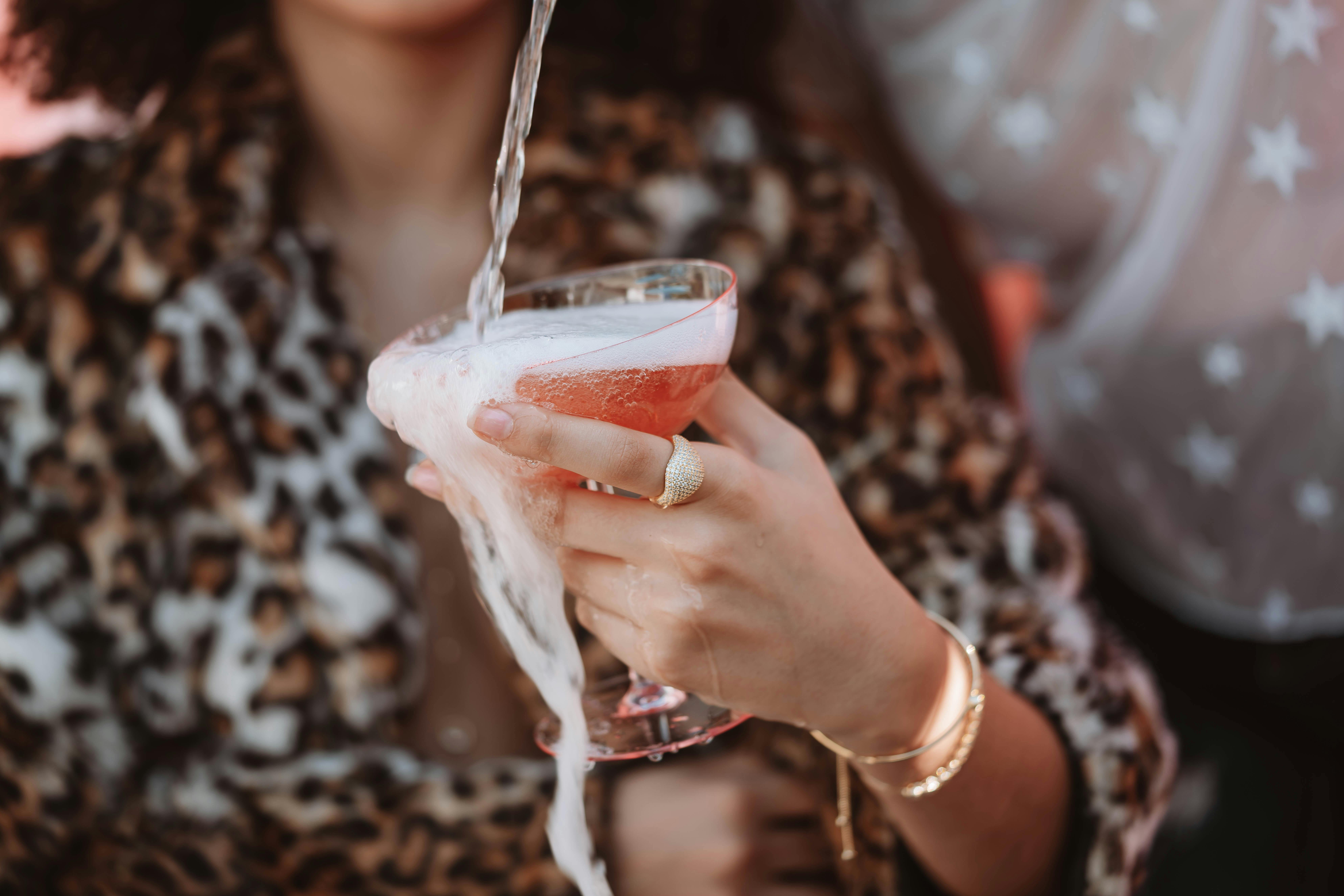 Close-up of a woman in leopard print pouring a luxury cocktail with foam overflowing.