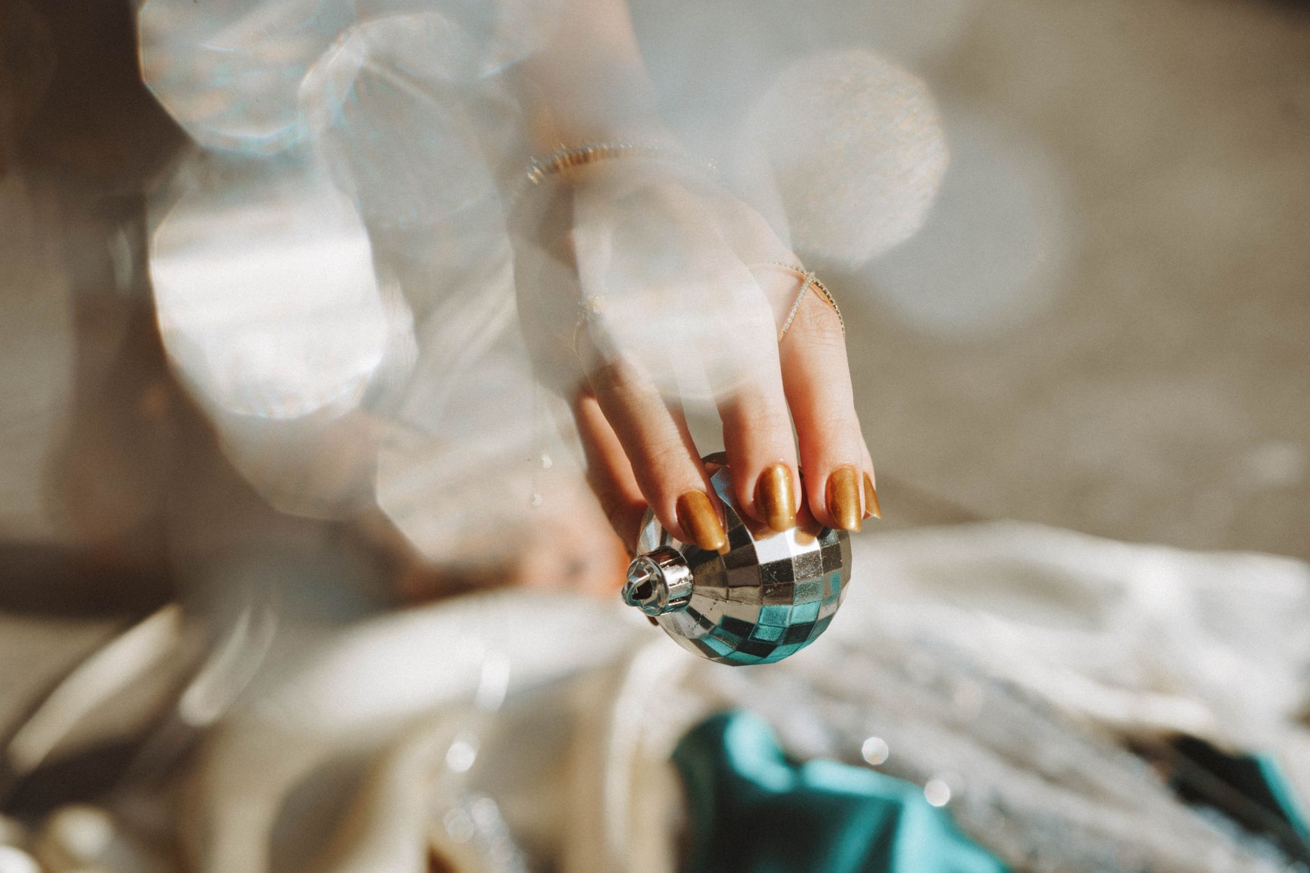 A close-up of a hand with manicured nails holding a shiny Christmas bauble, capturing holiday elegance.