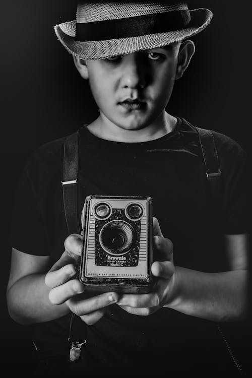Grayscale Photo of a Boy Holding a Vintage Camera