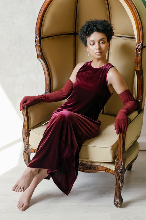 Woman Wearing a Maroon Velvet Dress Sitting on a Wooden Armchair