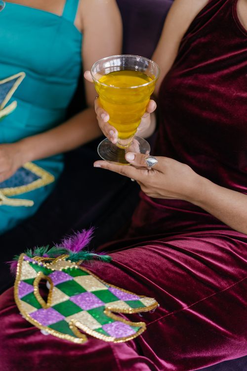 Free Two women in elegant dresses hold a festive drink and Mardi Gras mask, celebrating indoors. Stock Photo