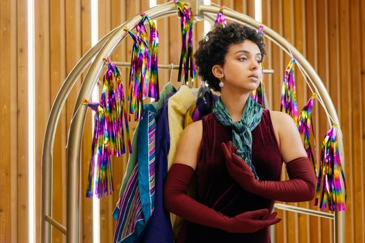 Fashionable woman in maroon dress posing with rainbow decor indoors, conveying elegance and style.