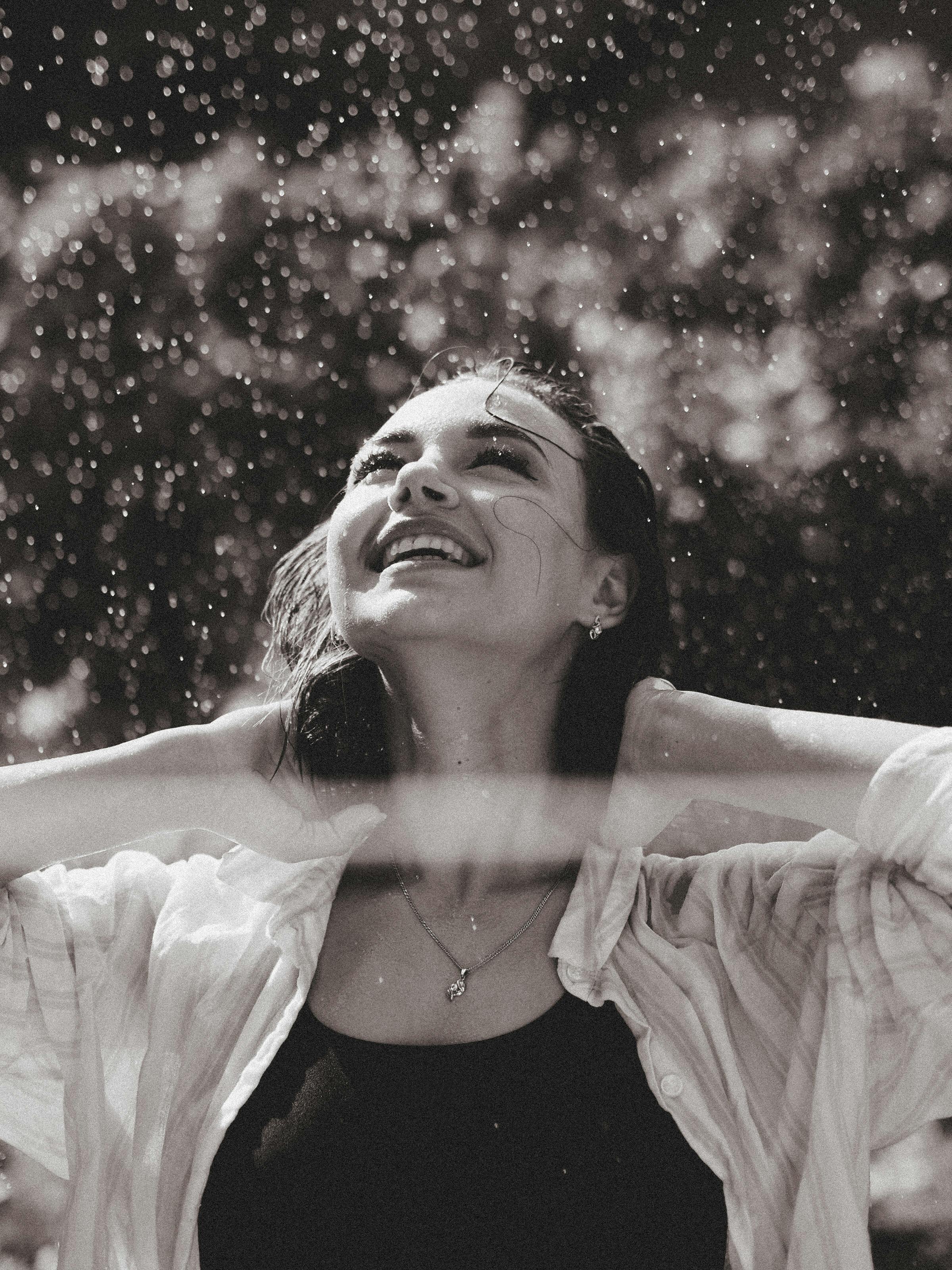 A young woman smiles freely as she enjoys the rain, captured in a monochrome setting.