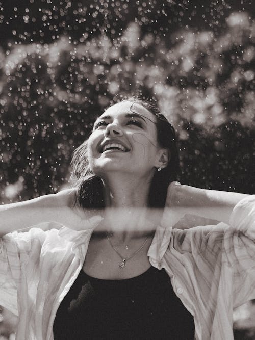 Grayscale Photo of a Woman Smiling while under the Rain