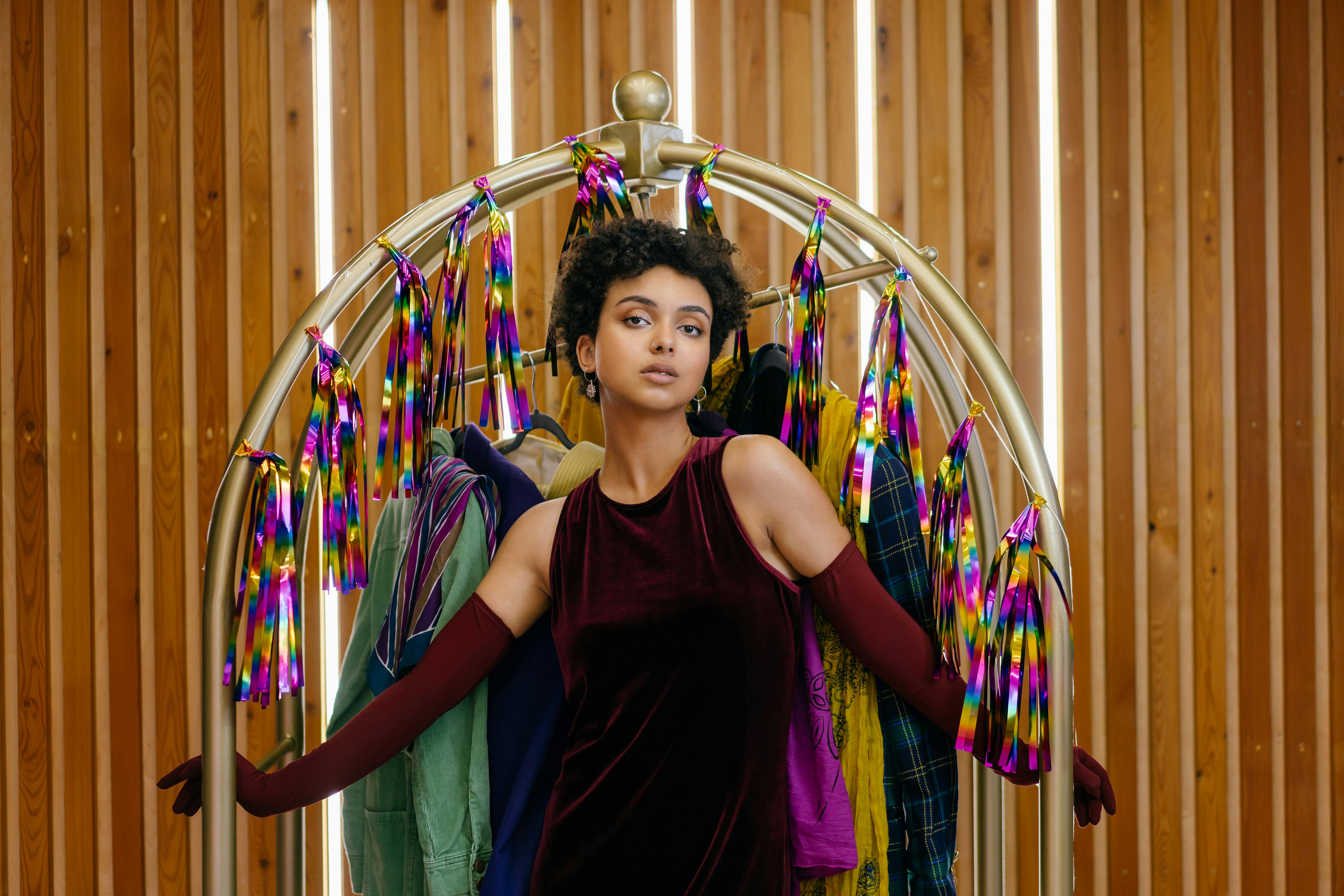 Stylish woman posing in maroon velvet dress with a vibrant fashion background indoors.