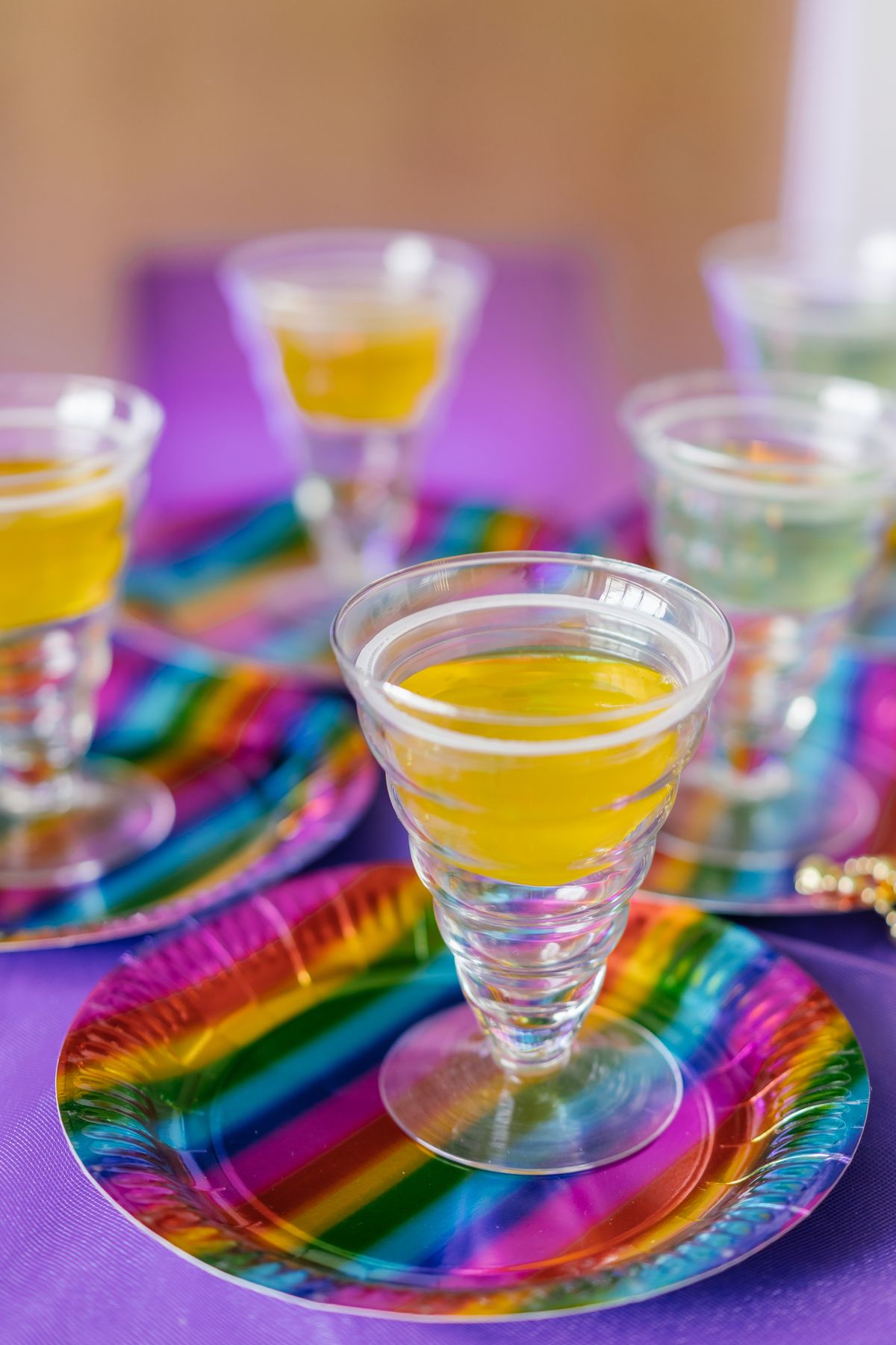 Brightly colored drinks in clear glasses on vibrant rainbow plates