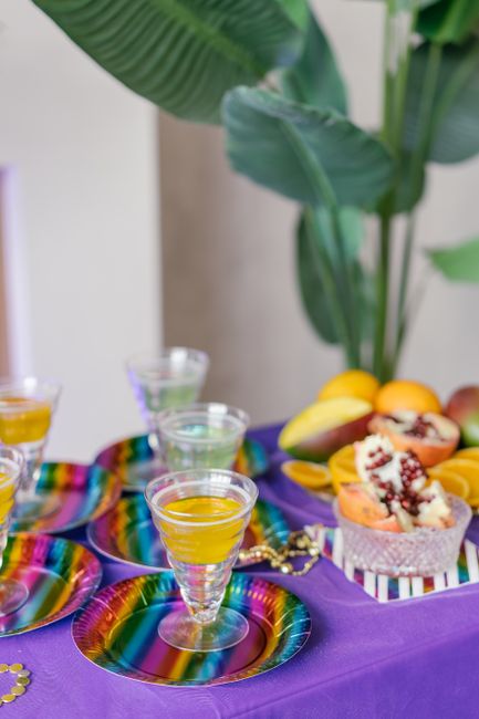 A tall glass of golden mango juice with ice cubes, garnished with a lime wedge, next to two halved ripe mangoes on a wooden board.