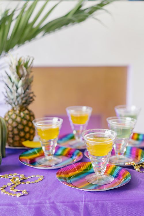 Free Colorful party setup with glasses of juice on rainbow plates and a pineapple for a festive vibe. Stock Photo