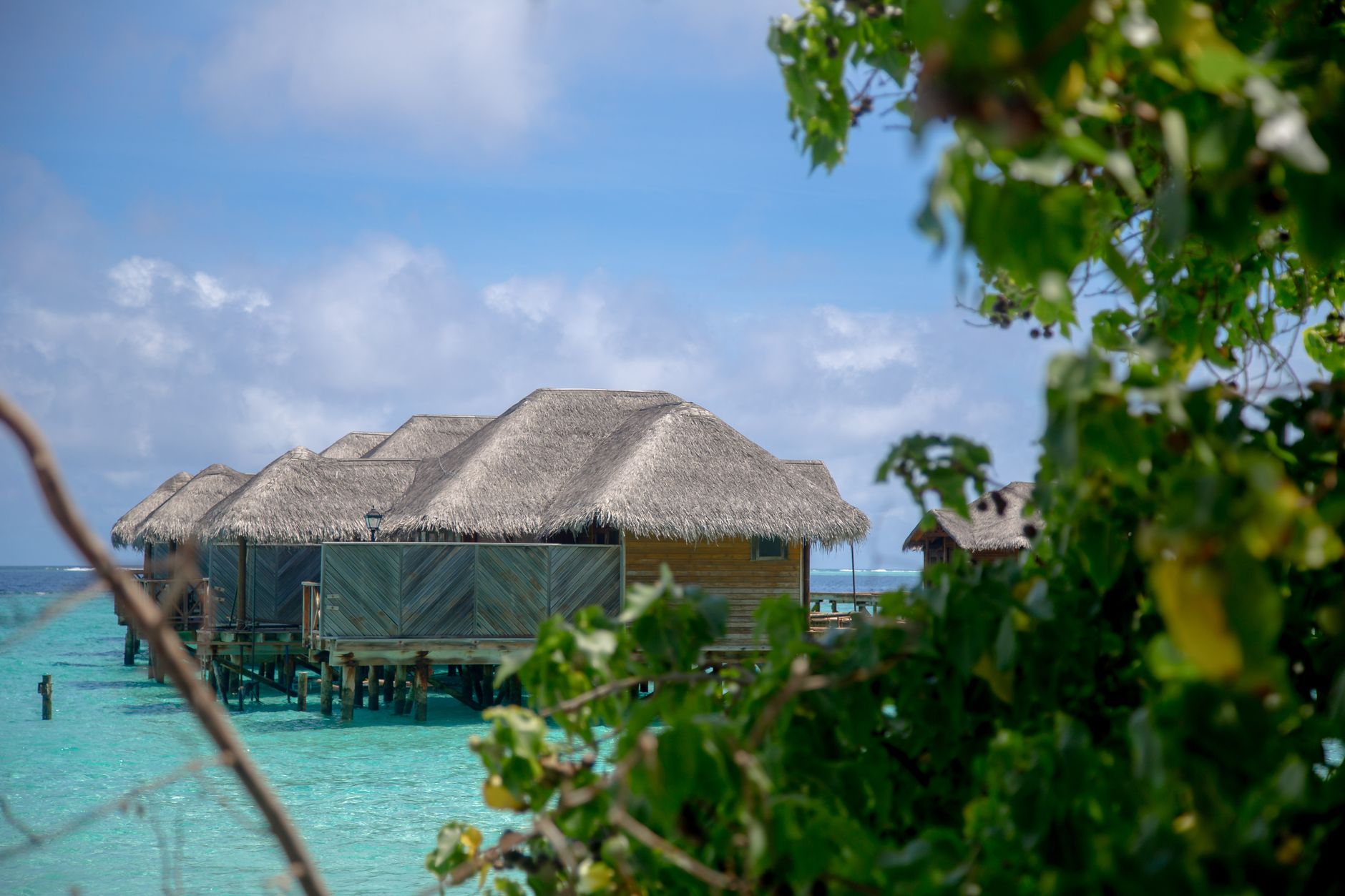 Tropical wooden villas with thatched roofs set on crystal-clear waters in a luxury resort setting.