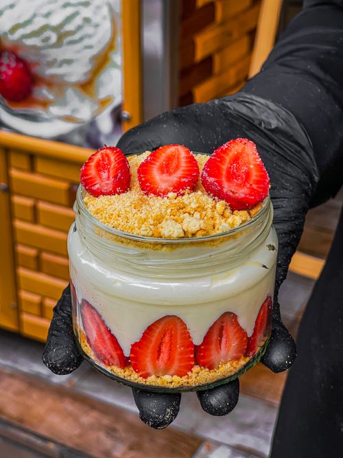 Free Close-up of a creamy strawberry tiramisu dessert in a glass jar held by a gloved hand. Stock Photo