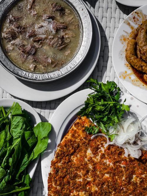 Free A variety of delicious Asian dishes including lahmacun and soup served on white plates with herbs and vegetables. Stock Photo