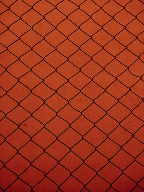 Free Detailed image of a chain link fence against a vibrant orange wall, highlighting geometric patterns. Stock Photo