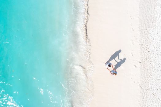 A couple holding hands on a pristine beach in Maldives, captured from above, showcasing turquoise waters and white sand.