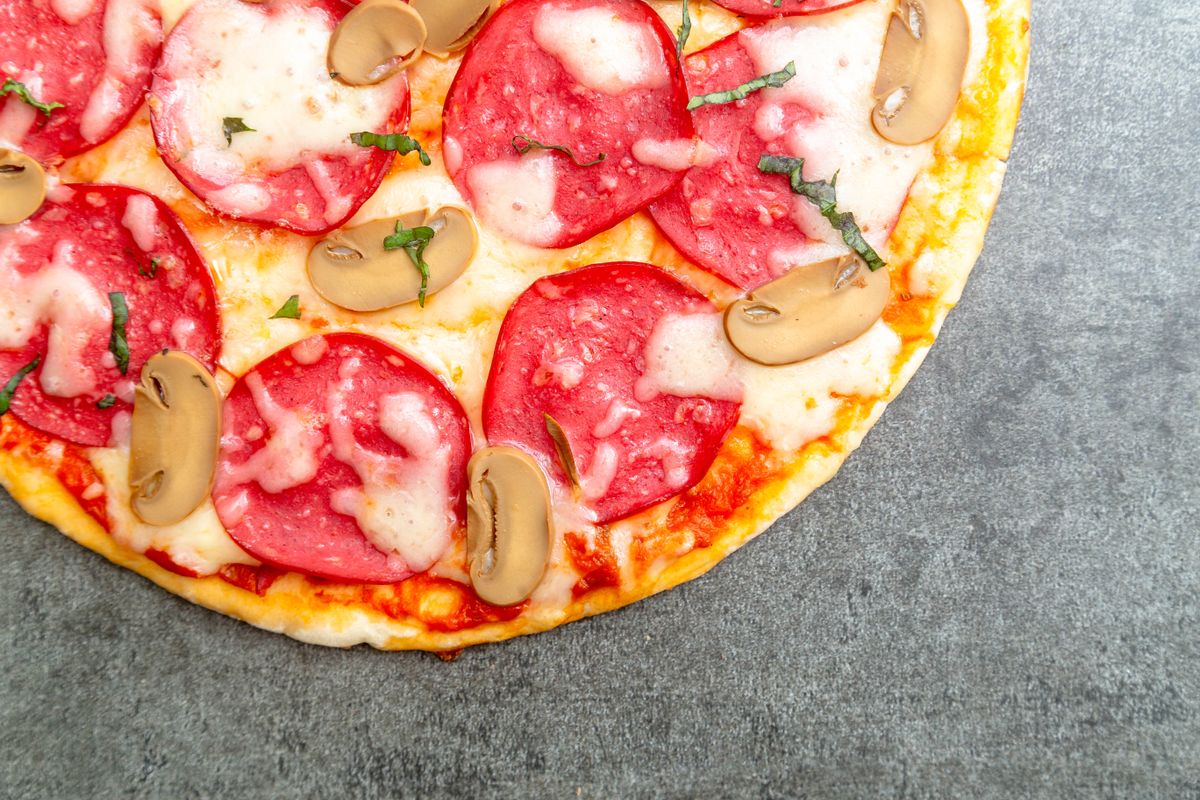 Pizza topped with large salami slices, halved button mushrooms, melted cheese and herbs