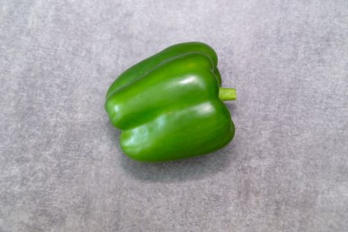Free A vibrant green bell pepper displayed on a minimalistic gray surface, perfect for healthy food themes. Stock Photo