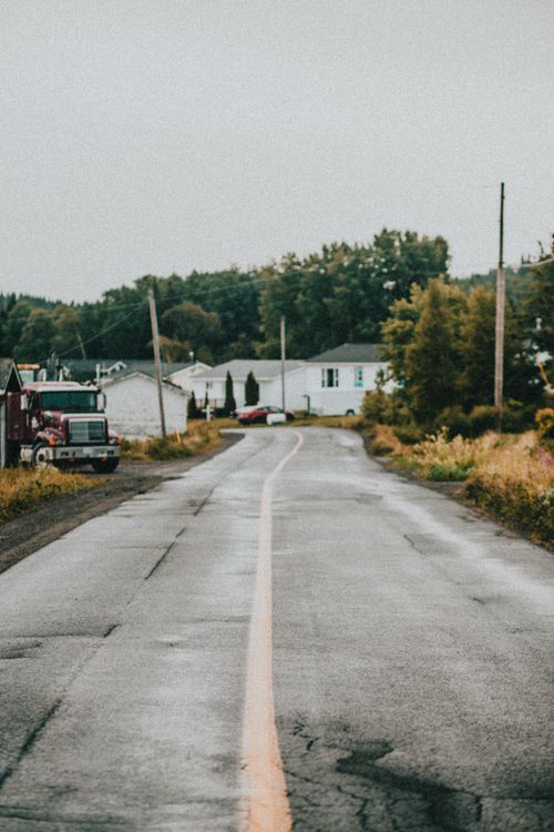 Free A wet rural road leading through a quiet neighborhood lined with houses and trucks. Stock Photo