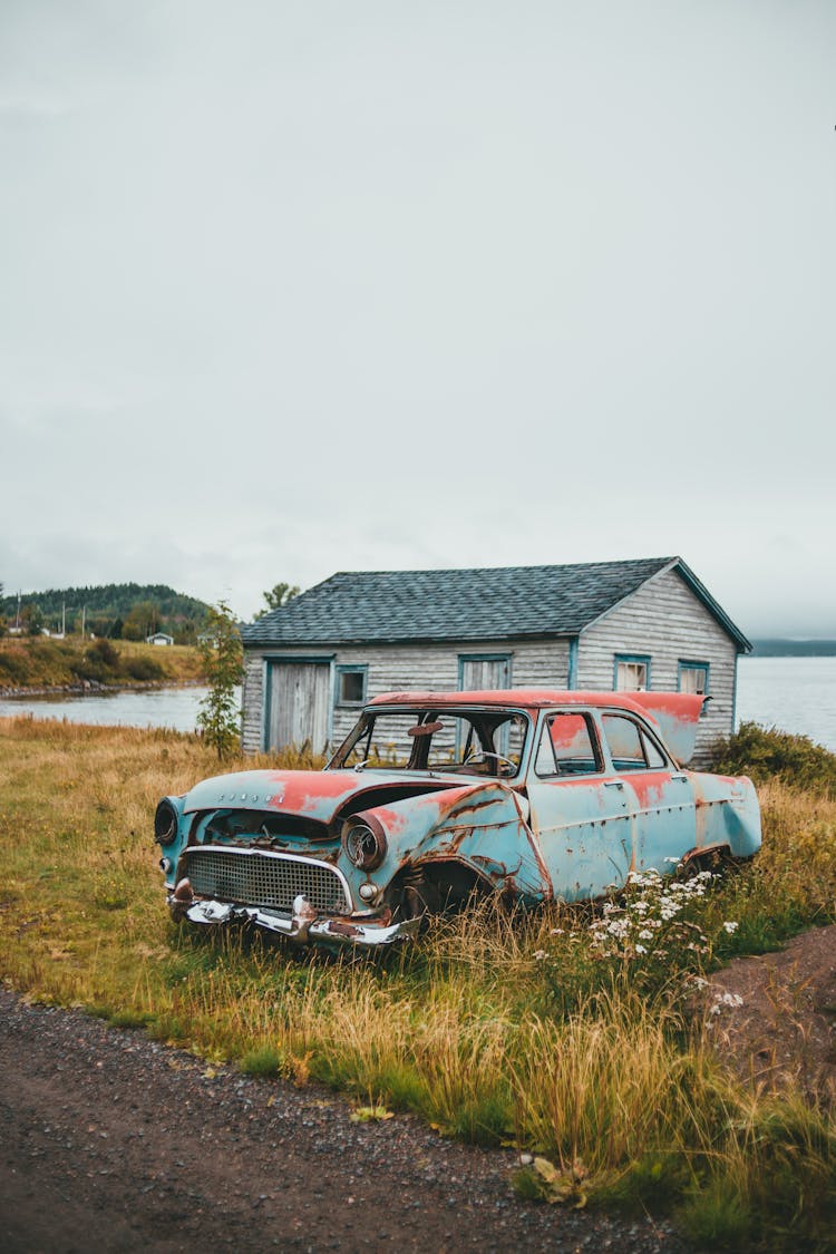 Rusted Car Wreck Parked By Shed In Grass