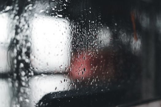 Close-up of raindrops on a window with a blurred background, capturing a moody ambiance.
