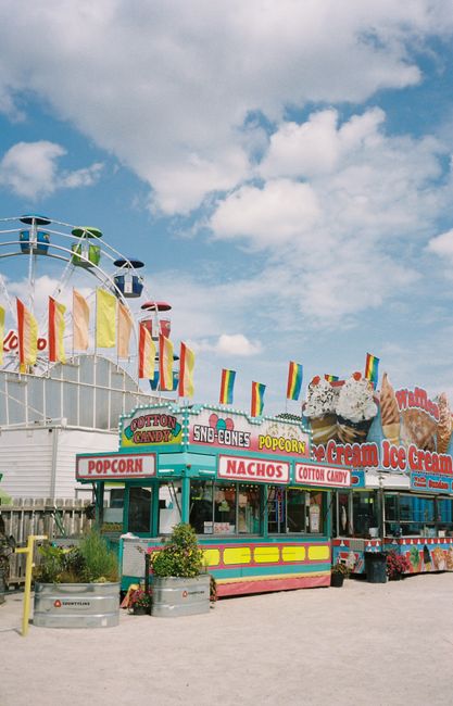Vibrant carnival food stalls offering snacks like popcorn and ice cream under a clear blue sky.