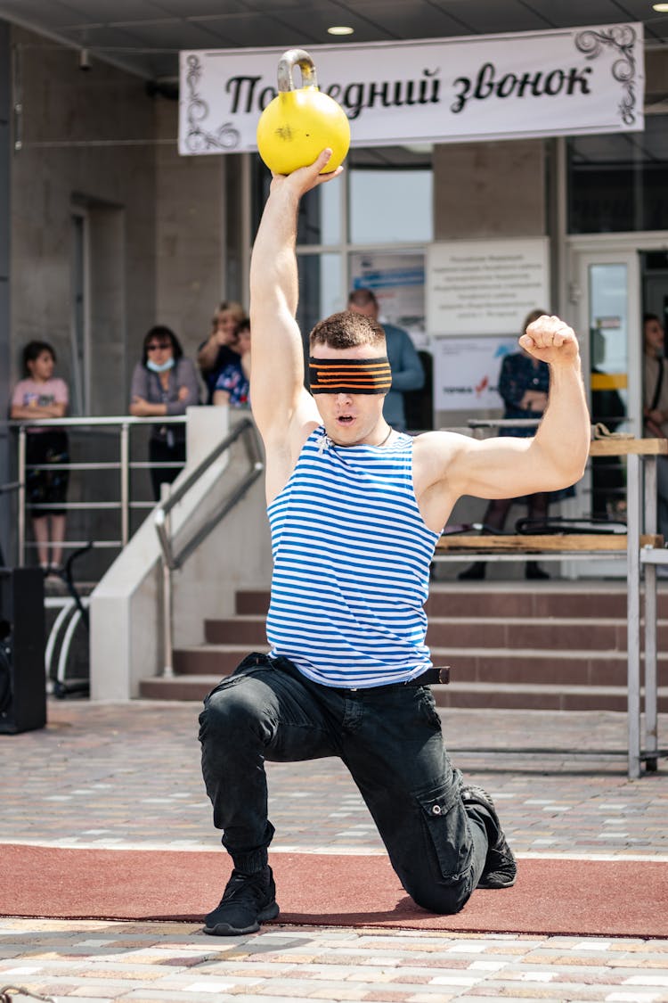 A Blindfolded Man Lifting A Kettle Bell