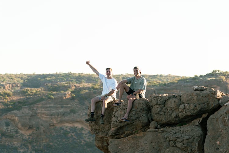 Men Sitting On Edge Of A Cliff