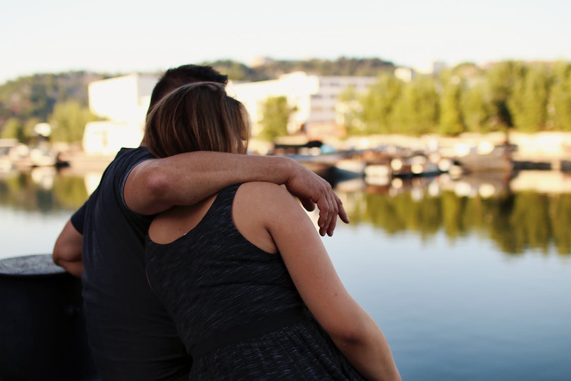 Free Man and Woman Sitting in Front of Body of Water Stock Photo