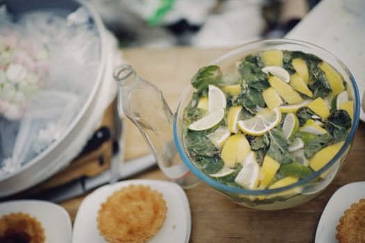 A close-up of a refreshing lemon and mint drink in a glass bowl with accompanying tarts.