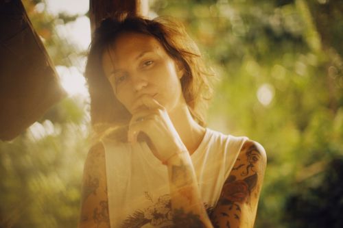 Free A contemplative woman with tattoos in a sleeveless shirt, immersed in soft natural lighting and blurred background. Stock Photo