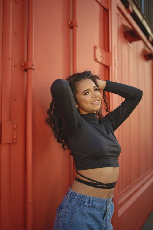 Free Woman in black crop top smiling and posing against a vibrant red wall outdoors. Stock Photo