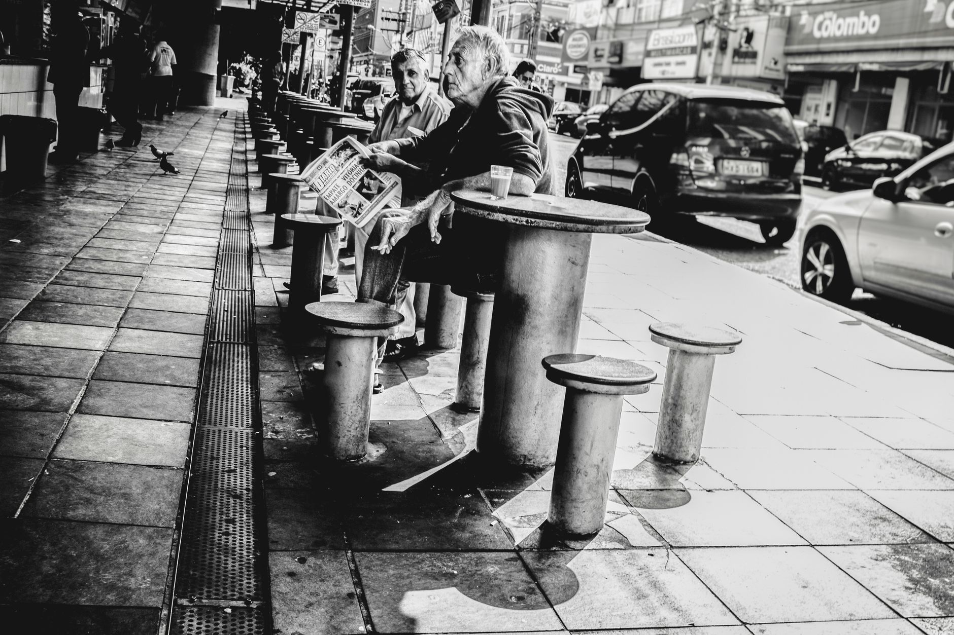 Black and white image of elderly men sitting at a café table on a busy street.