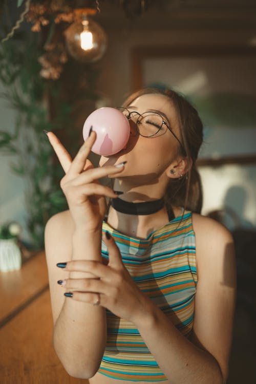Free A Woman in Striped Shirt Blowing a Bubble Gum Stock Photo