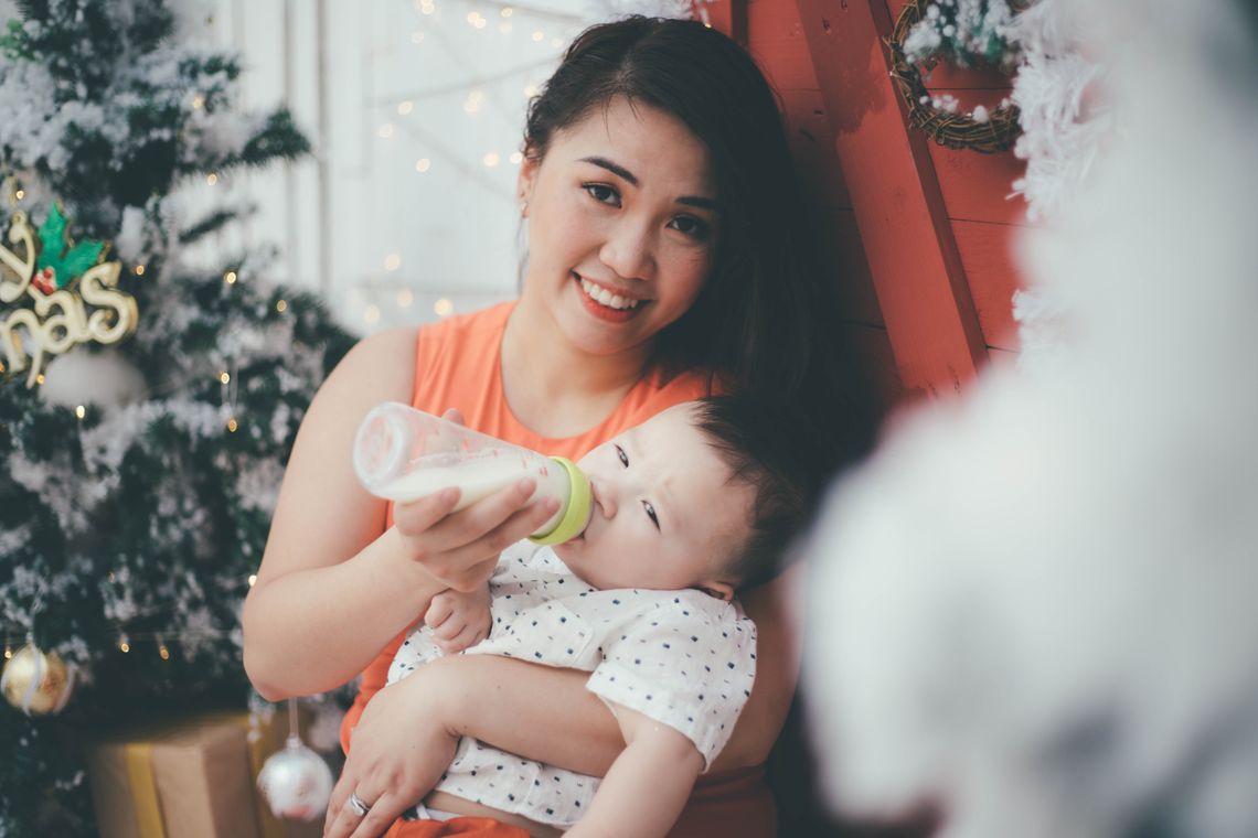 Smiling mother bottle feeding her baby indoors with her face clearly visible