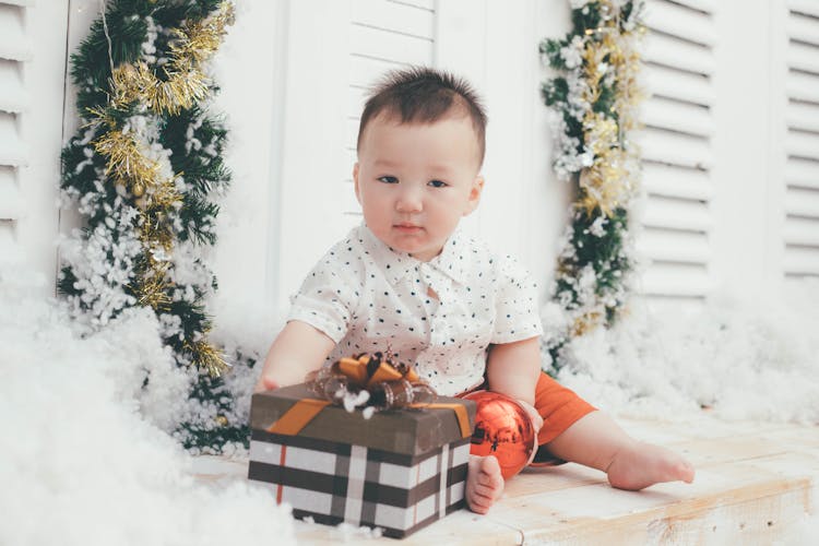 Baby In White And Blue Polka Dot Shirt Playing A Wrapped Box