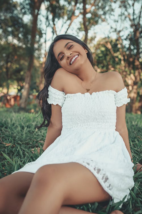 Smiling Woman in White Off Shoulder Dress Sitting on Grass