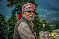 一位戴着眼镜和传统帽子的老人在自然环境中展示文化服饰