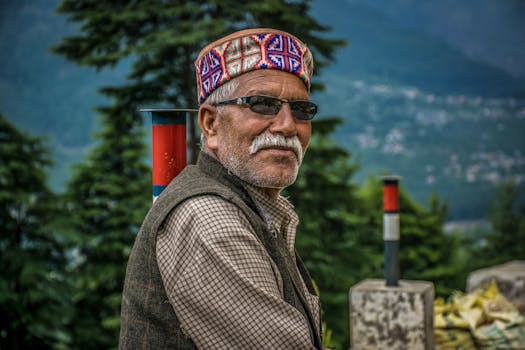 一位戴着眼镜和传统帽子的老人在自然环境中展示文化服饰