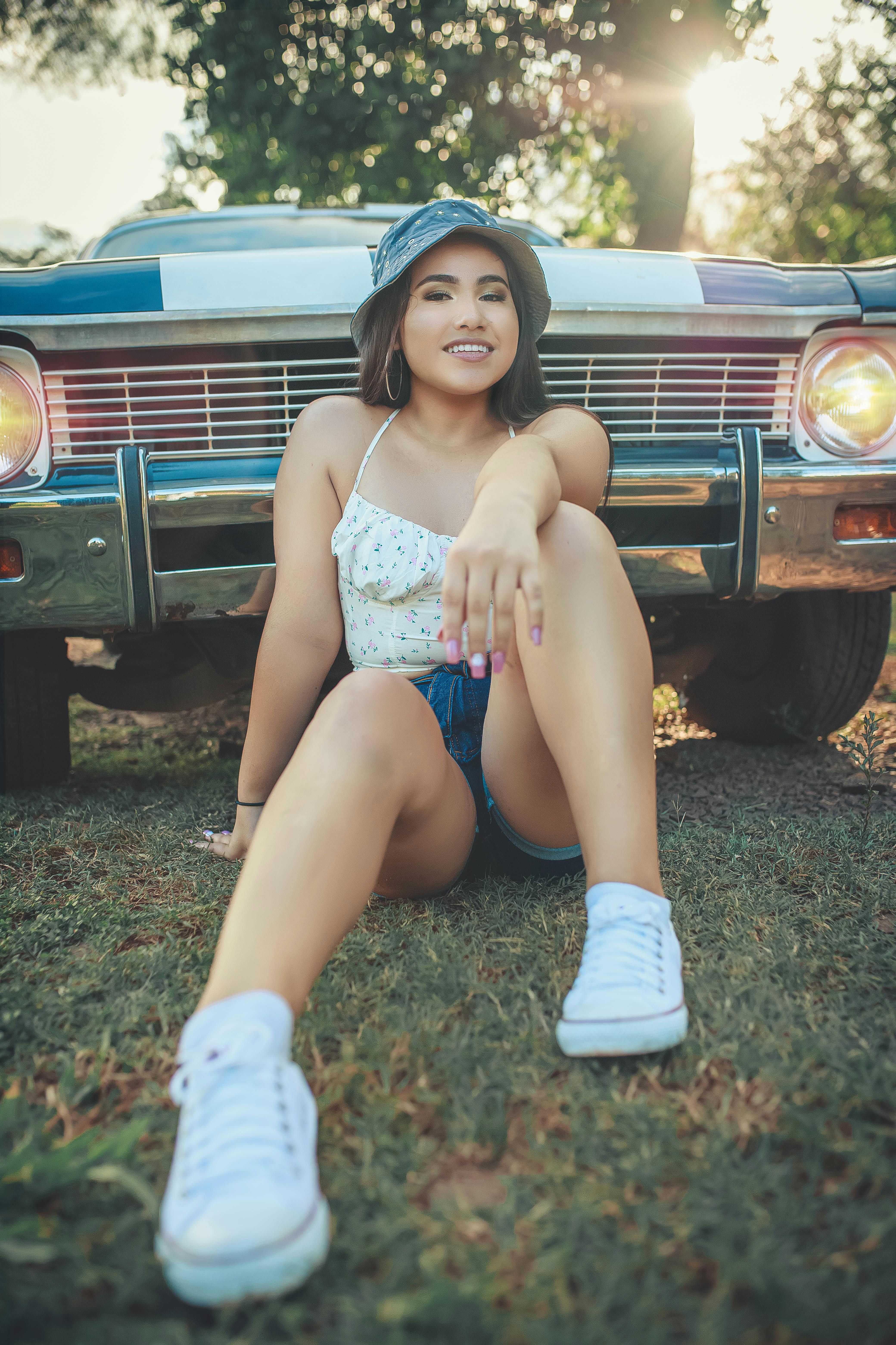 Young woman in denim shorts poses casually by vintage car outdoors in Paraguay.