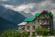 这座现代化的山屋拥有绿色屋顶，在多云的天空下背靠白雪皑皑的山峰