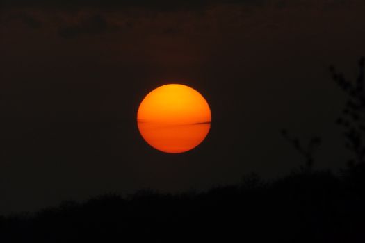 Vibrant sunset with bold orange sun against dark silhouette outdoors