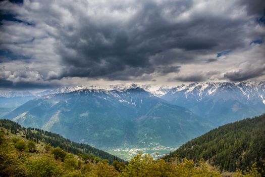 Majestic mountain range with snow-capped peaks under dramatic clouds, showcasing natural beauty.