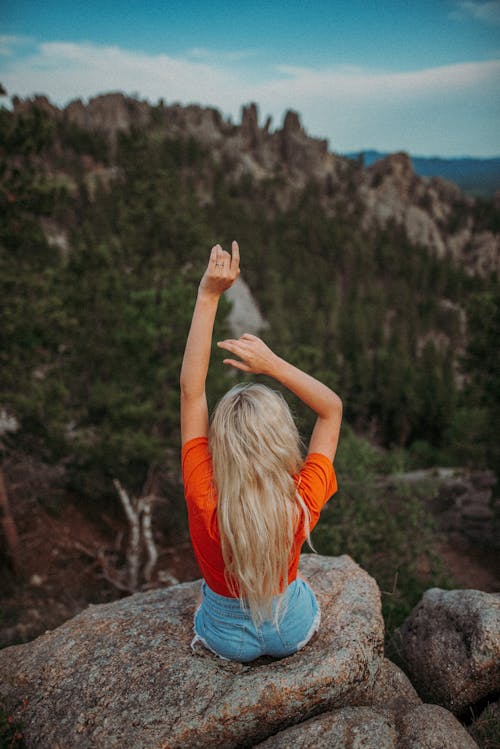 A Woman in Orange Shirt Sitting on a Cliff Rock