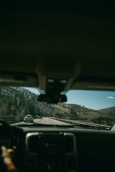 View from inside a car driving through a scenic mountain highway under clear skies.
