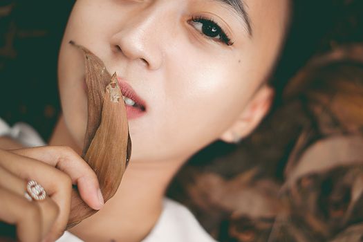 A detailed close-up of a person holding a dry leaf near their face, captured outdoors with soft focus.