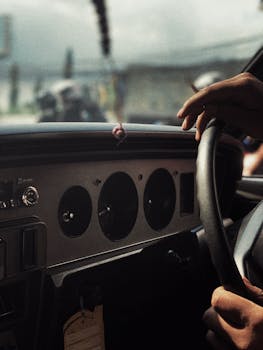 Close-up view of a vintage car dashboard and steering wheel, hands visible.